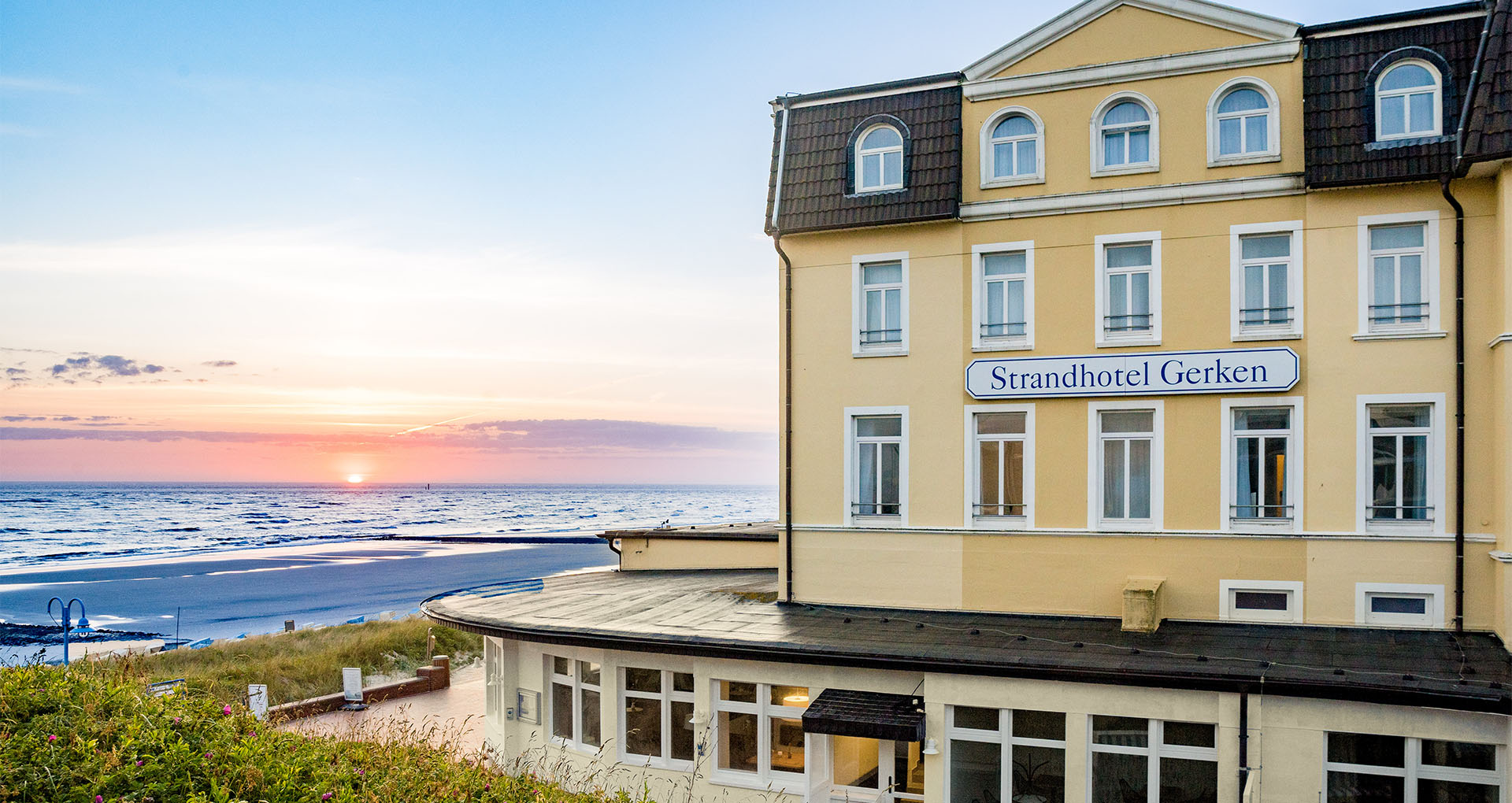 Strandhotel Gerken auf Wangerooge mit Sonnenuntergang im Hintergrund und Blick auf das Meer und Strand